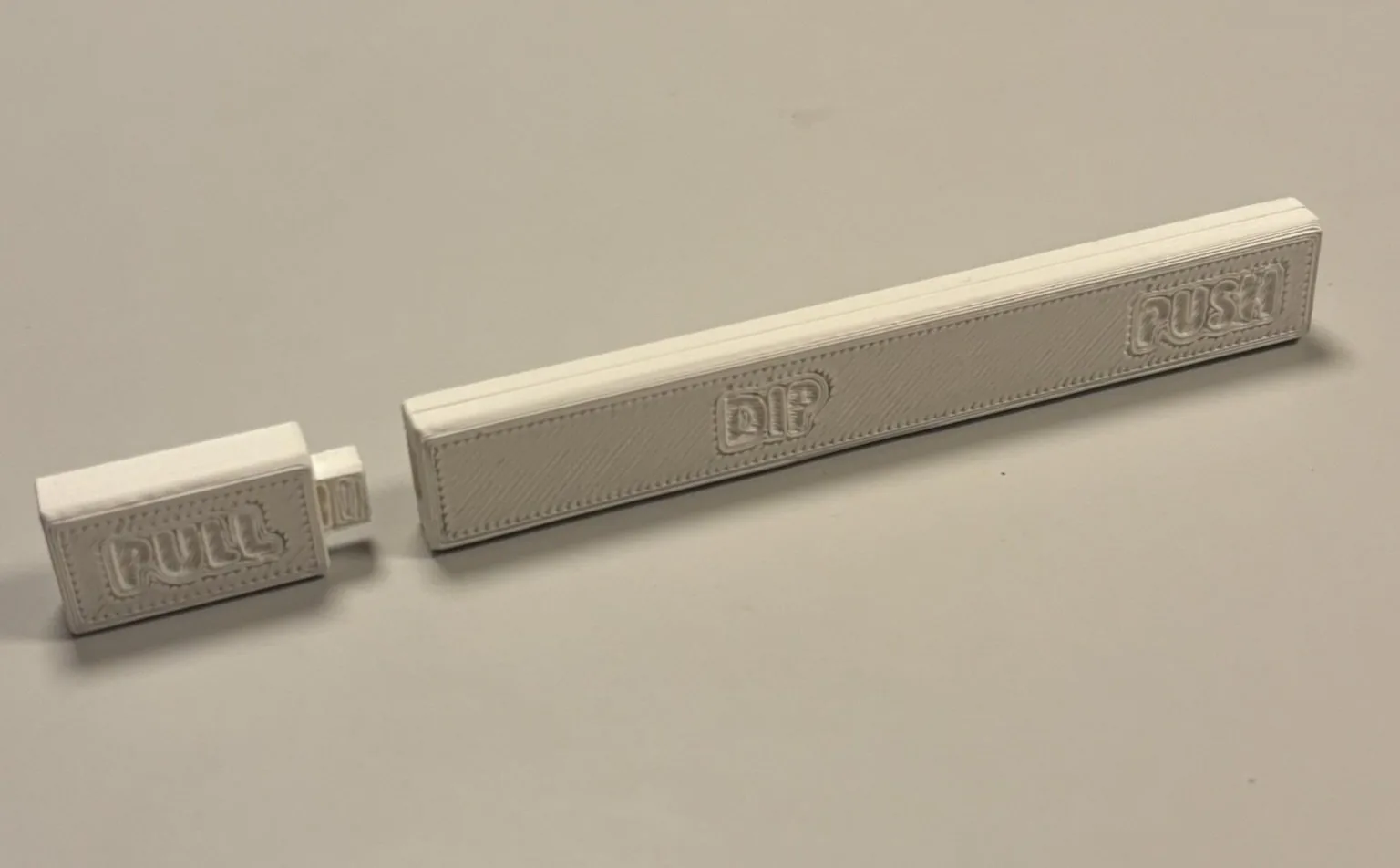 The 3D-printed PeePen prototype lying on a table, cap pulled off. The body is embossed with DIP and PUSH, the cap with PULL.