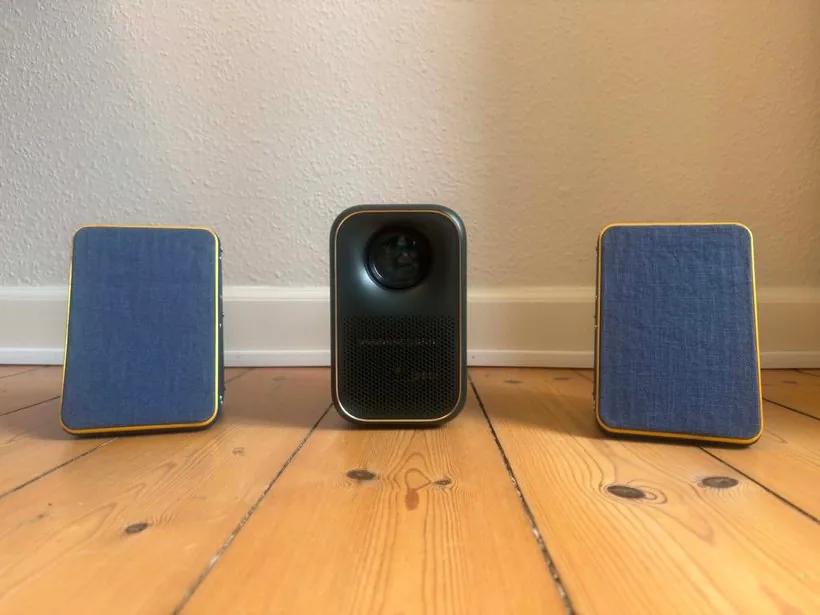 Final prototype: projector between two blue fabric-fronted speakers on a wooden floor