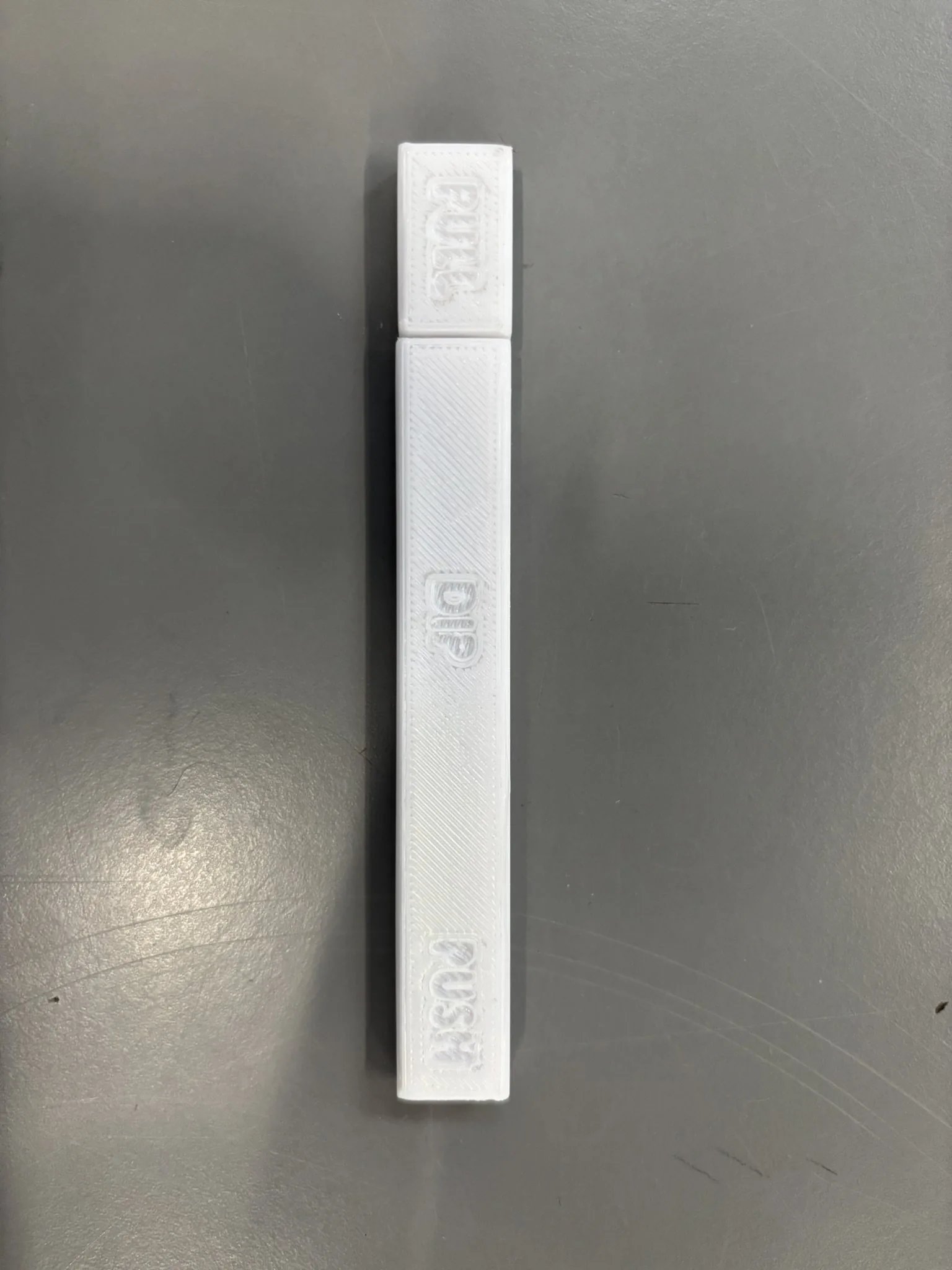 The finished 3D-printed PeePen seen from above on a grey surface, with PULL on the cap, DIP in the middle and PUSH at the far end.